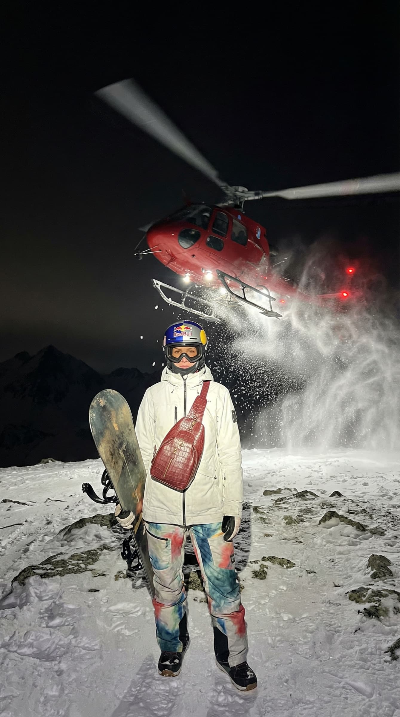 Red GENA sling bag worn on a night summit beneath a helicopter